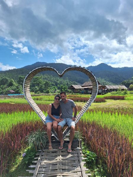 A couple in the metal heart sculpture over red rice fields - lifeonwheel.com