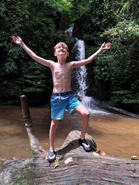 A boy celebrating on a fallen log by the falls - lifeonwheel.com